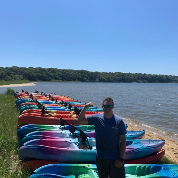 A man waits by the beach with a group of kayaks waiting to give a tour of Cape Cod by water