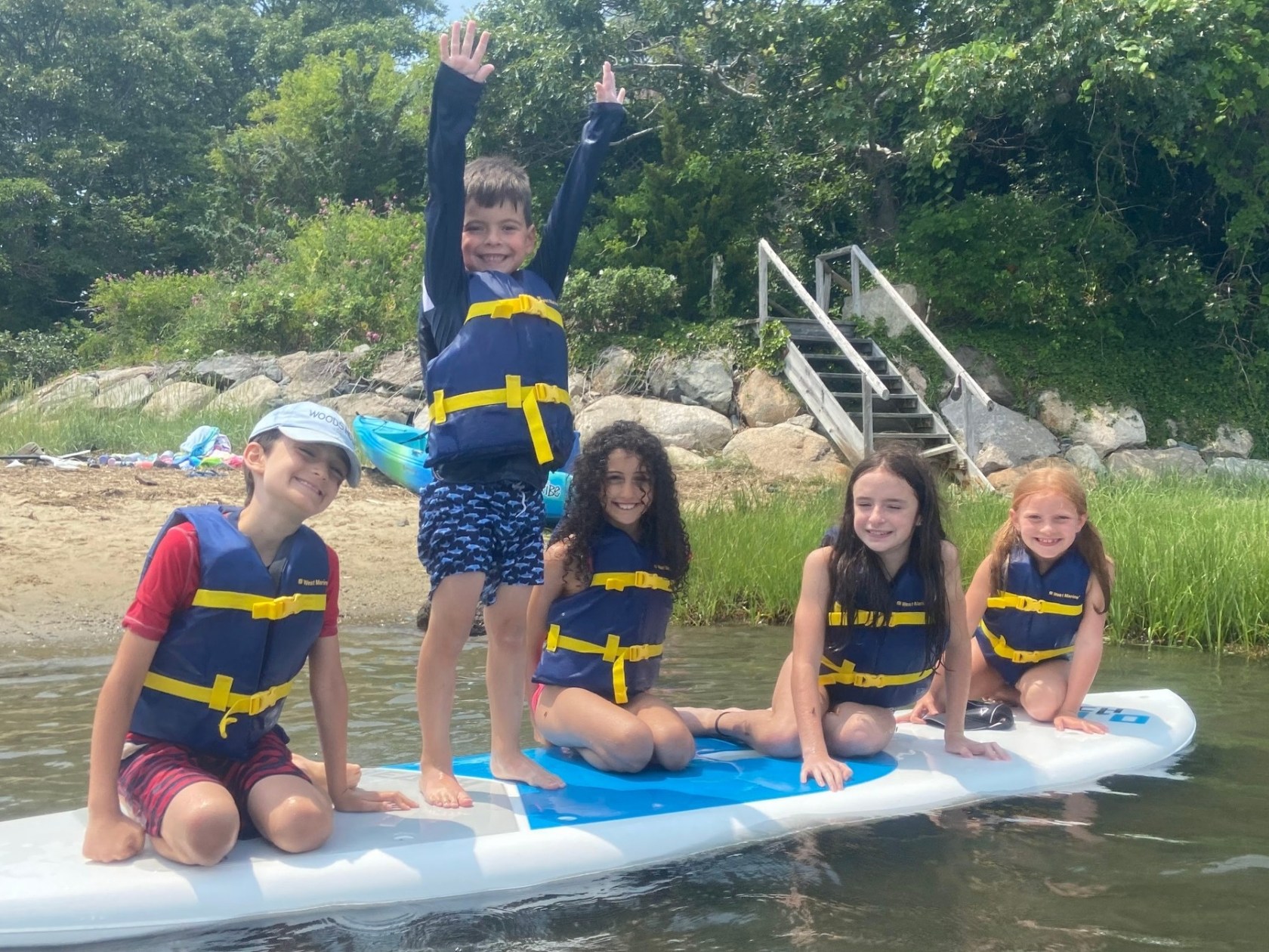 Five children enjoy a sunny Cape Cod day paddle boarding through Mashpee during Kids Camp