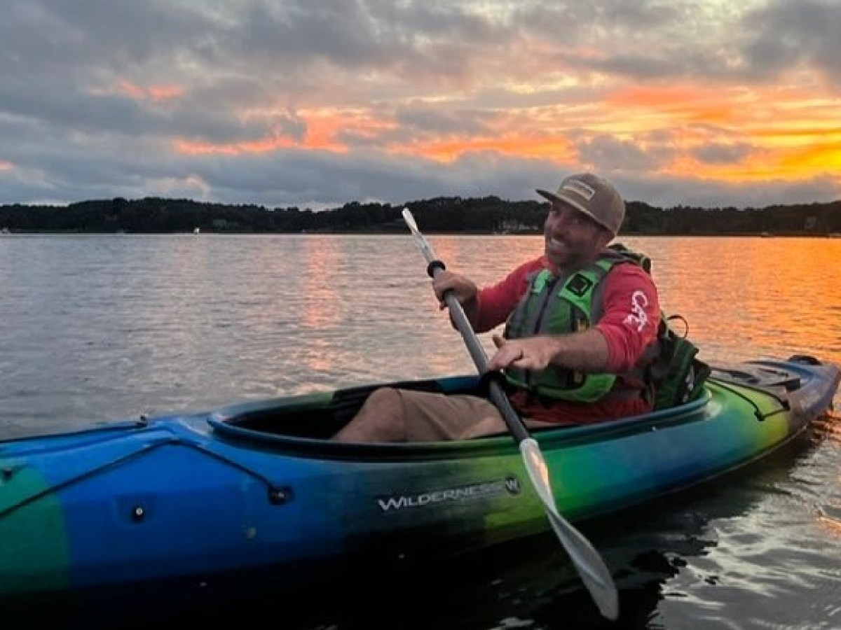 A man smiling with the sunset behind him in a kayak from RideAway Adventures