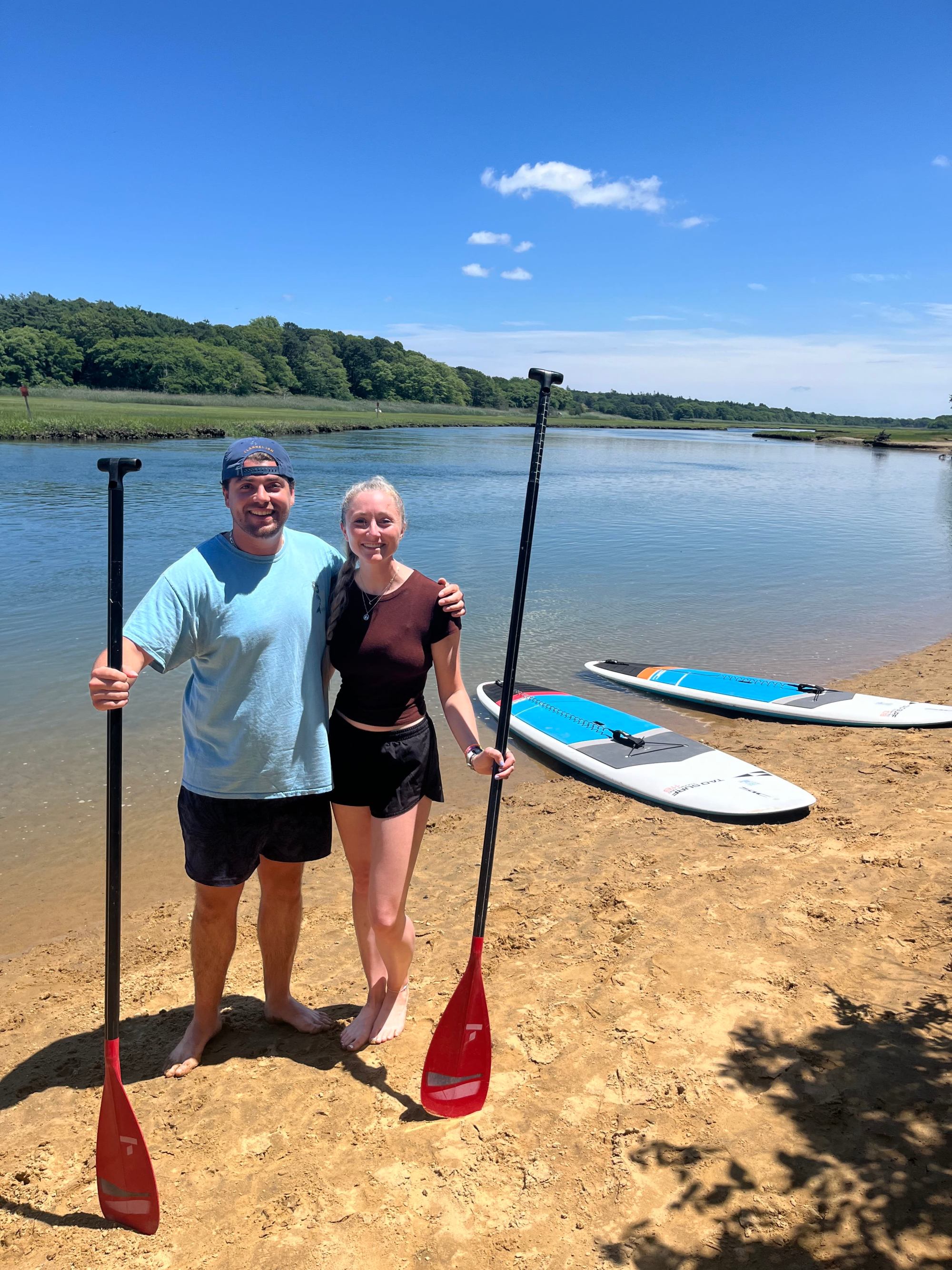 RideAway Adventures Sandwich Creek – 2024-06-24-12-28-44-165-a6ii2 A happy couple standing on a beach with standup paddleboards after a tour in Sandwich with Rideaway Adventures
