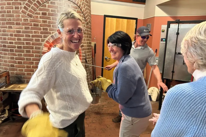 People smiling and engaging in glassblowing workshop with brick kiln.